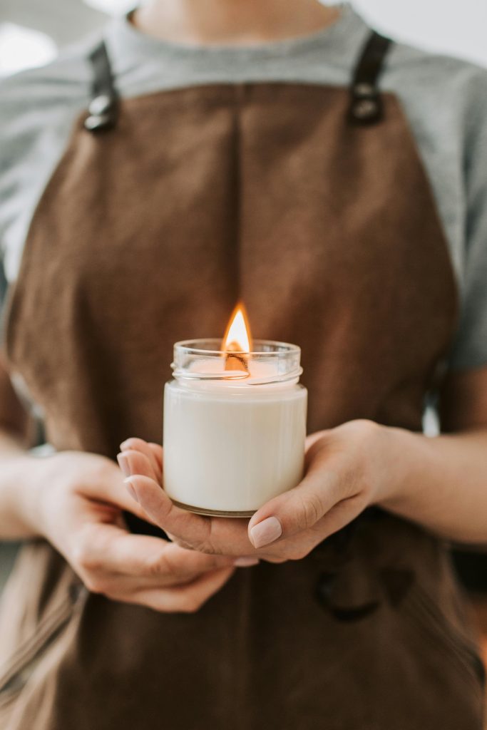 Warm ambient lighting with a focus on handmade candle in a jar held by a craftsman wearing an apron.